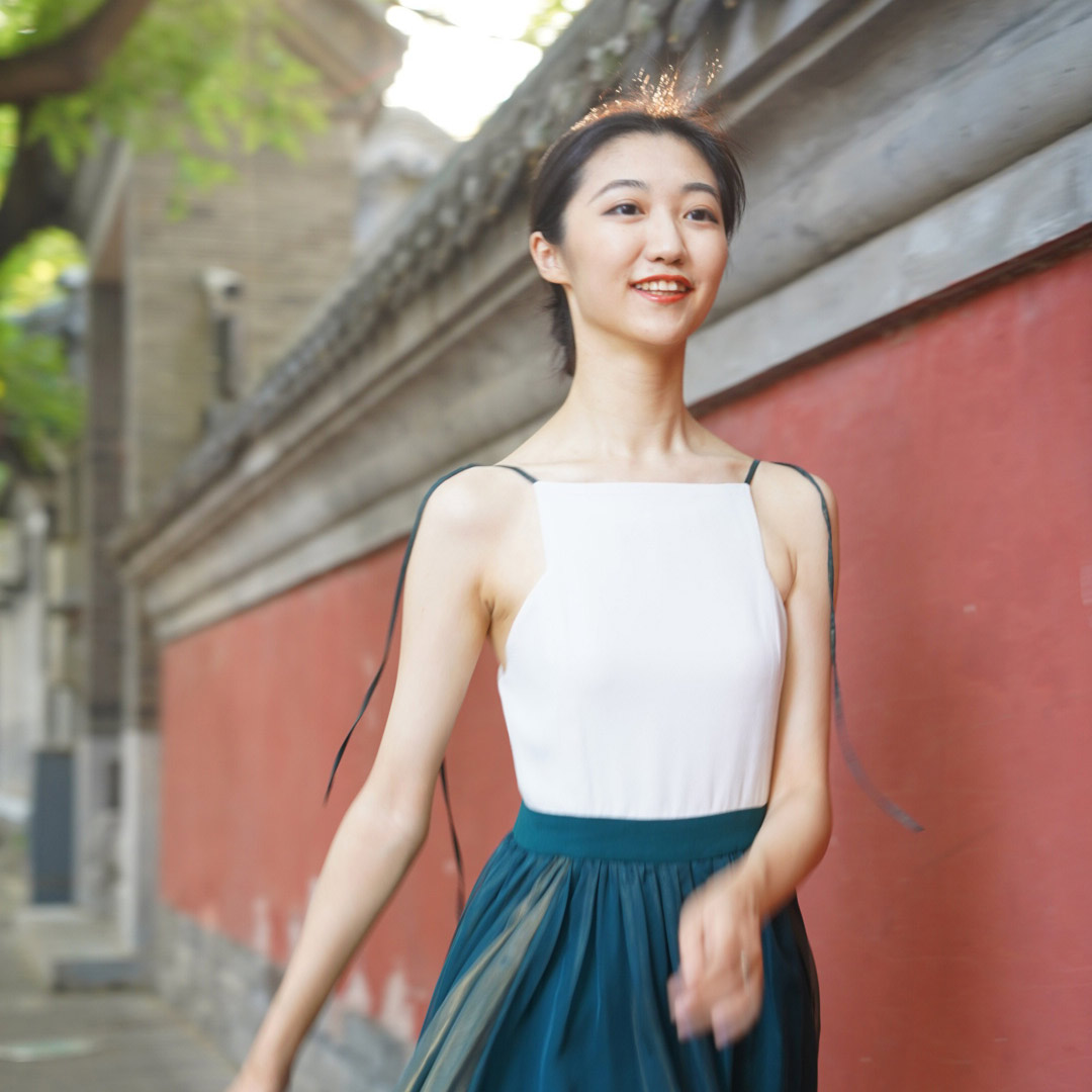 A young smiling Asian woman in a summer dress, walking down the sidewalk.