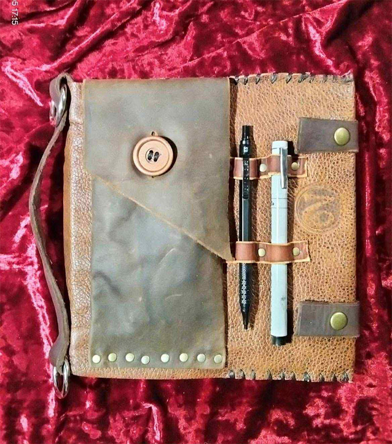 A handmade black and brown leather pencil holder with loops to hold pens and a small pocket with a button enclosure.