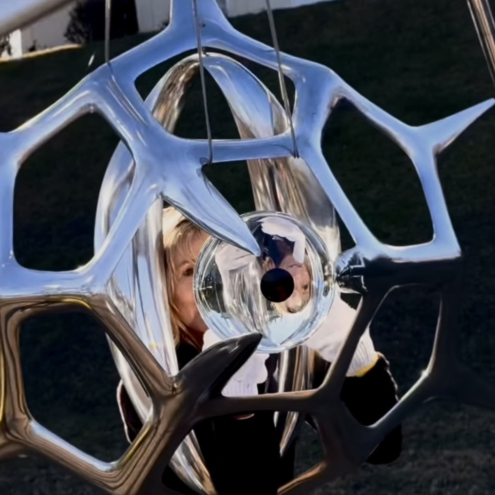 A woman amidst an abstract sculpture peering into an orb in the center.