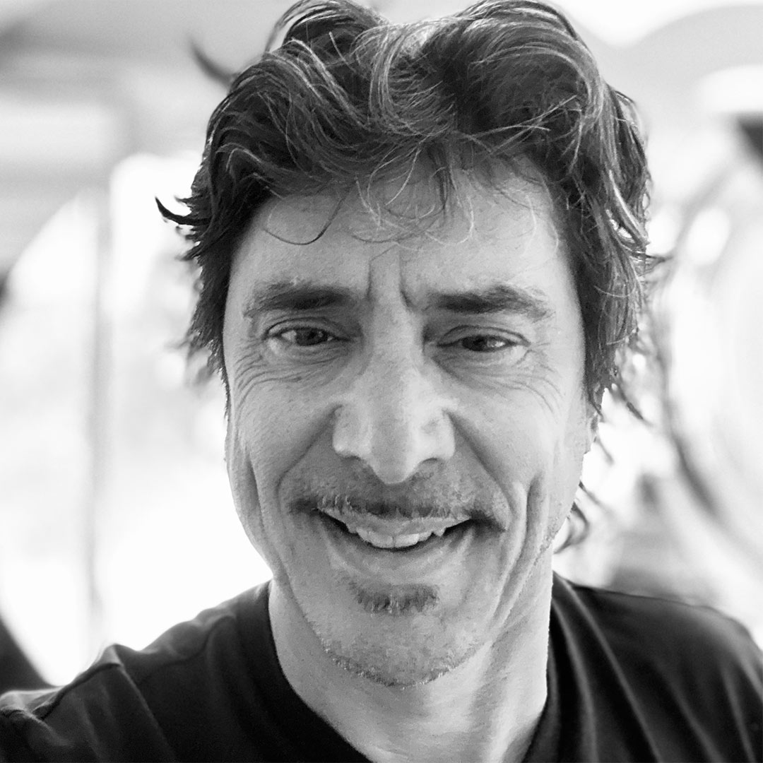 An older dark-haired man with a thin mustache, wearing a black T-shirt.