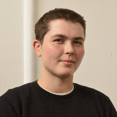 A youthful looking person with short cropped hair, wearing a black shirt.